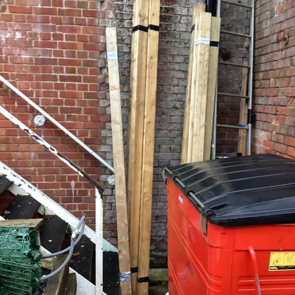 Three packs of 9ft timber leaning against a brick wall.
