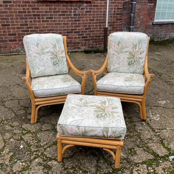 Vintage bamboo conservatory chairs and footstool set in a garden.