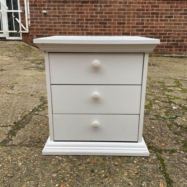 White three-drawer bedside cabinet in a bedroom setting.
