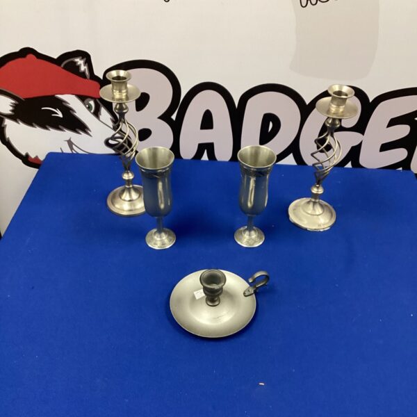 Vintage pewter candle holders and goblets on a dark surface.