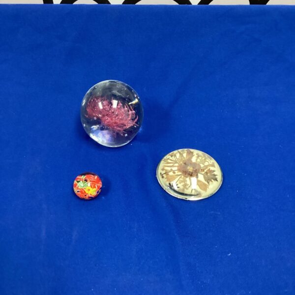 Vintage glass paperweights with floral, red, and abstract designs.