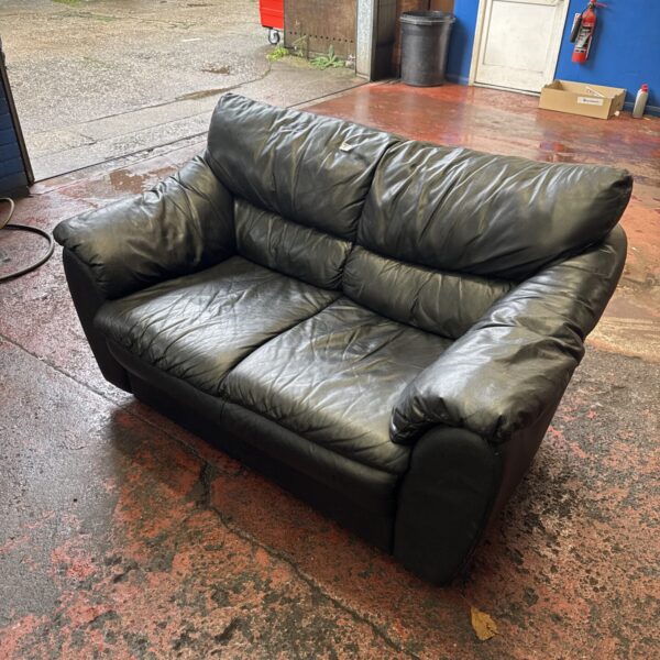 Dark brown leather two-seater sofa in a workshop setting.