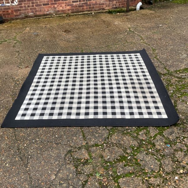 Black and white checkerboard Ikea Millinge rug on a paved surface.