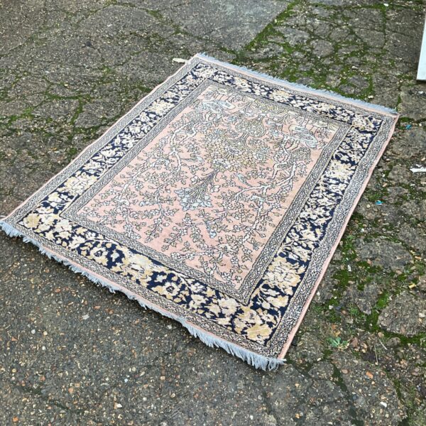 Vintage pink and blue floral rug with fringed edges.