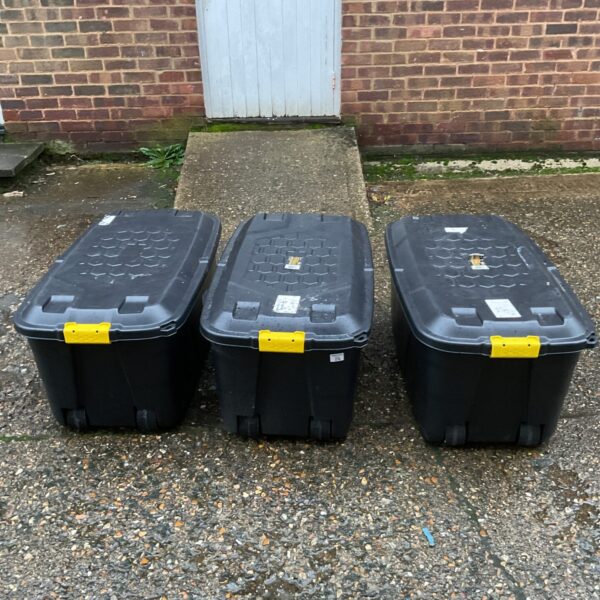 Three large wheeled storage boxes on a paved surface.