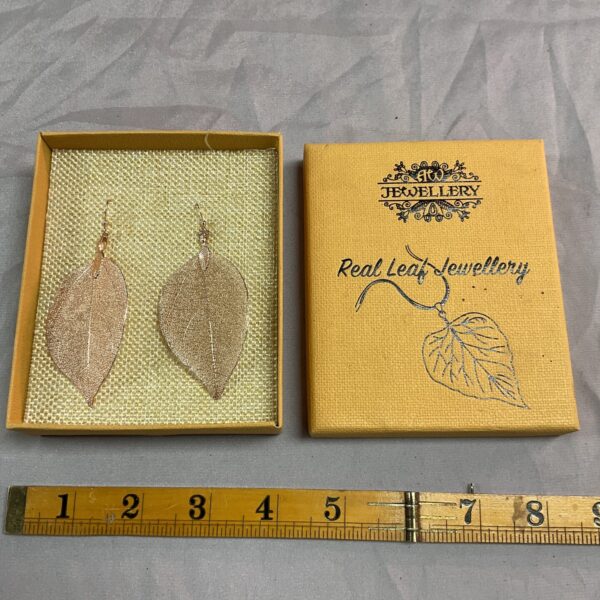 Close-up of delicate gilt leaf earrings with intricate veining.