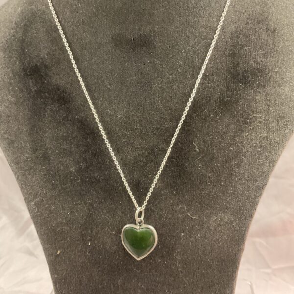 Close-up of silver necklace with green heart pendant.