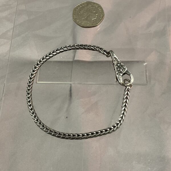 Close-up of a silver chain bracelet on a neutral surface.