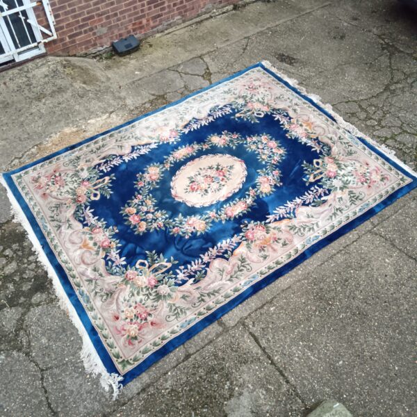 Large blue Chinese floral rug on a paved surface.