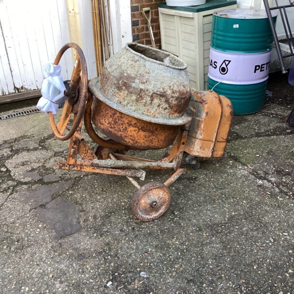Vintage petrol cement mixer in a garden setting.