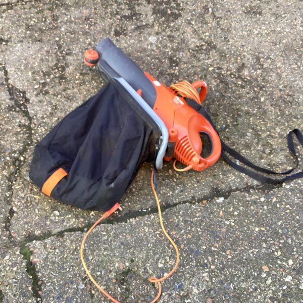Side view of a used Flymo electric lawn vacuum with collection bag.