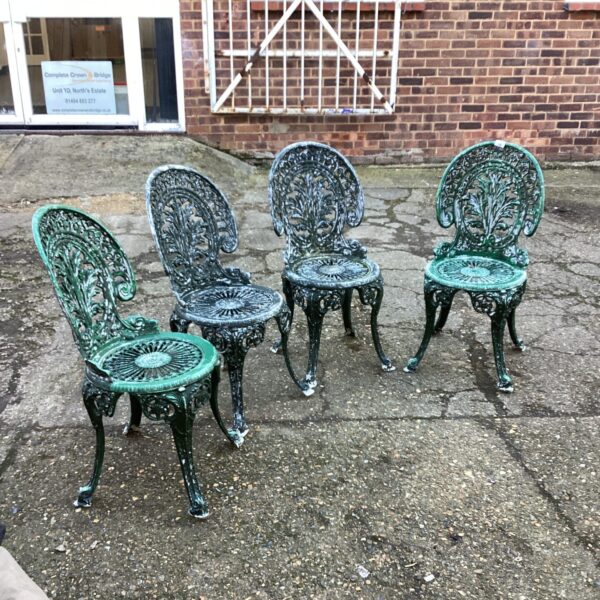 Four ornate metal garden chairs in a garden setting.