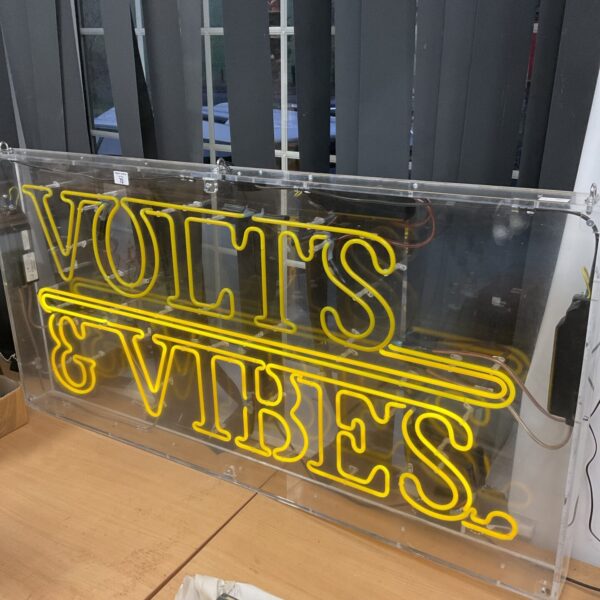 Vintage neon "Volts & Vibes" sign with vibrant illumination.