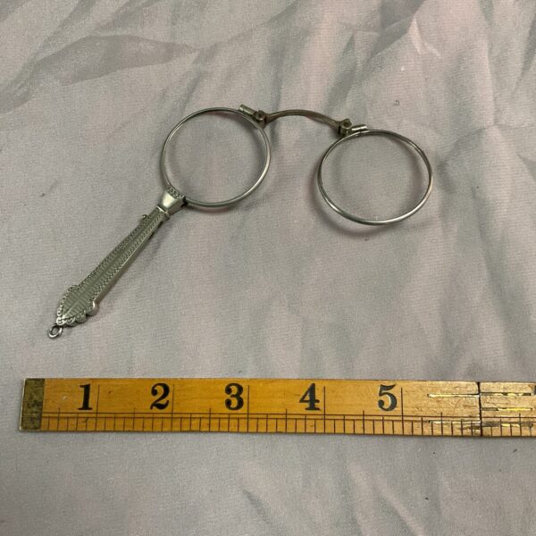 Antique whitemetal lorgnettes folded, shown with a ruler for scale.