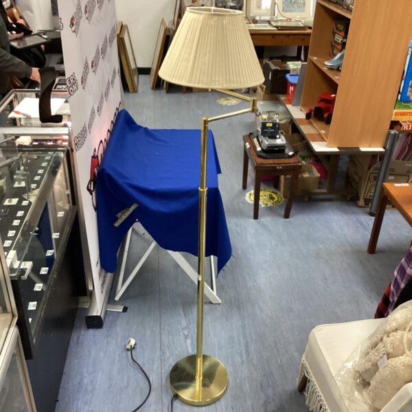 Tall brass standard lamp with adjustable head in a room.