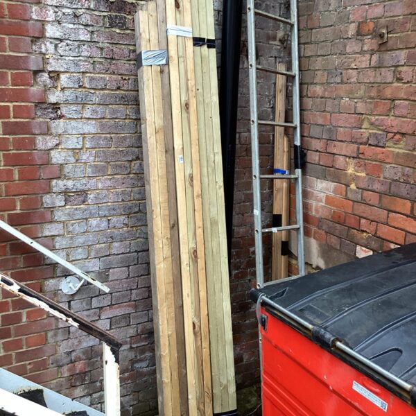 Three packs of 9ft timber leaning against a brick wall.