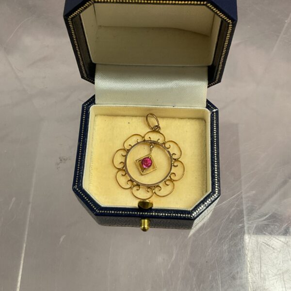 Close-up of a 9ct gold pendant with a red stone.