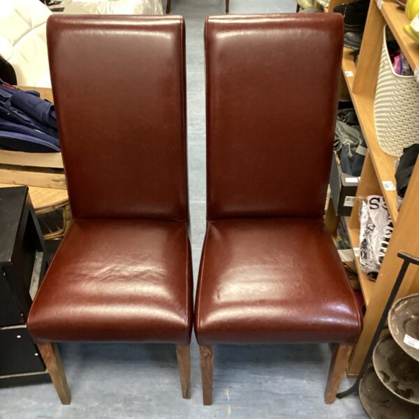 Two brown leather dining chairs with wooden legs.