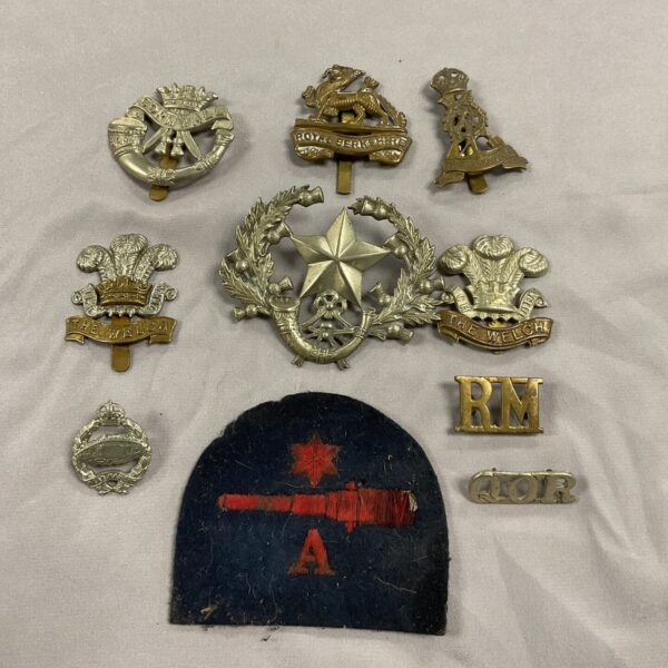 Collection of vintage military cap badges and a navy gunner patch.