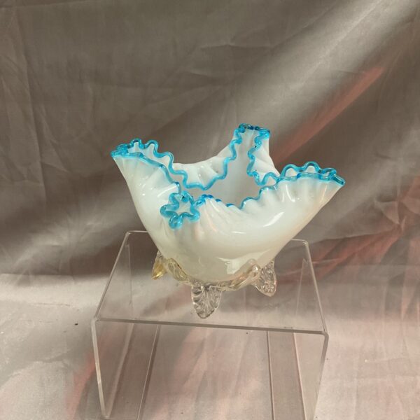 Antique milk glass handkerchief dish with blue rim and clear feet.