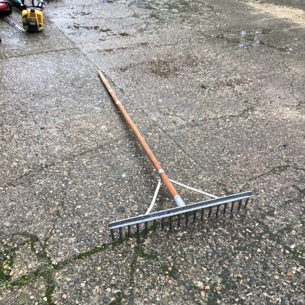Vintage straw rake with wooden handle and metal tines.