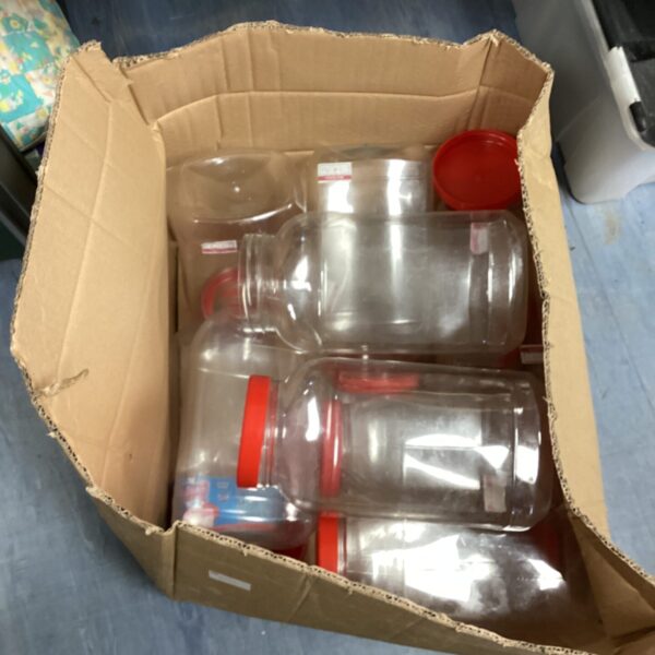 Several large plastic sweet jars with red lids in a cardboard box.