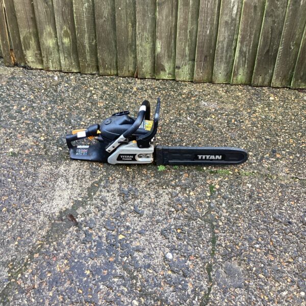 Side view of a used Titan petrol chainsaw for garden work.