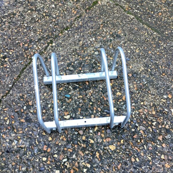 Metal bike rack for two bicycles, showing signs of wear.