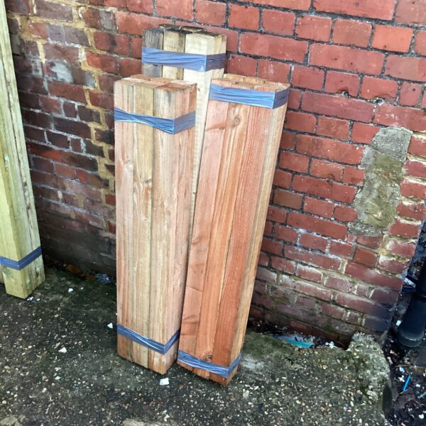 Three bundles of untreated timber stacked against a brick wall.
