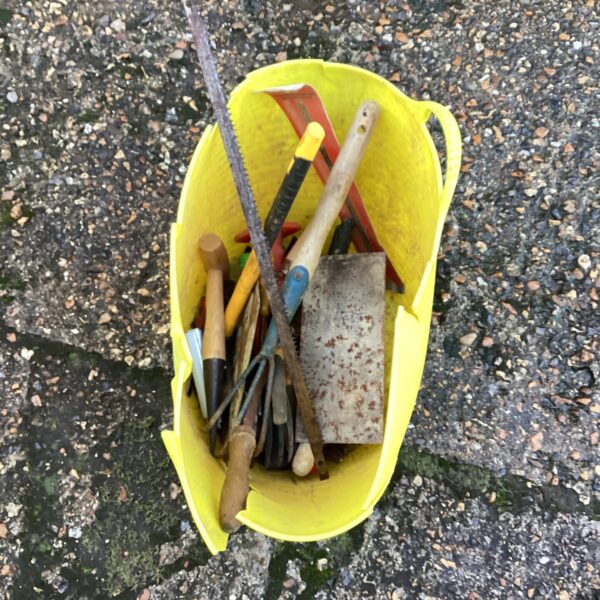 Basket of mixed vintage hand tools, including a saw and trowel.