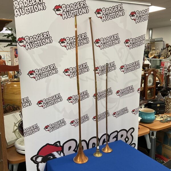 Three vintage copper coaching horns displayed on a patterned backdrop.