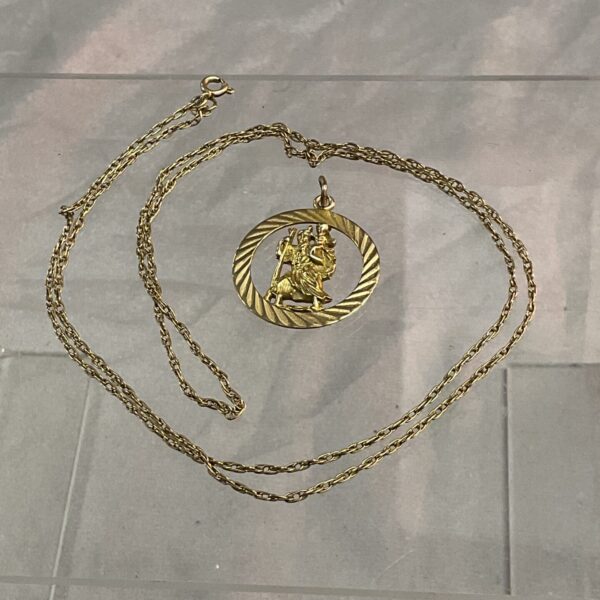 9ct gold St Christopher pendant and chain on a grey surface.