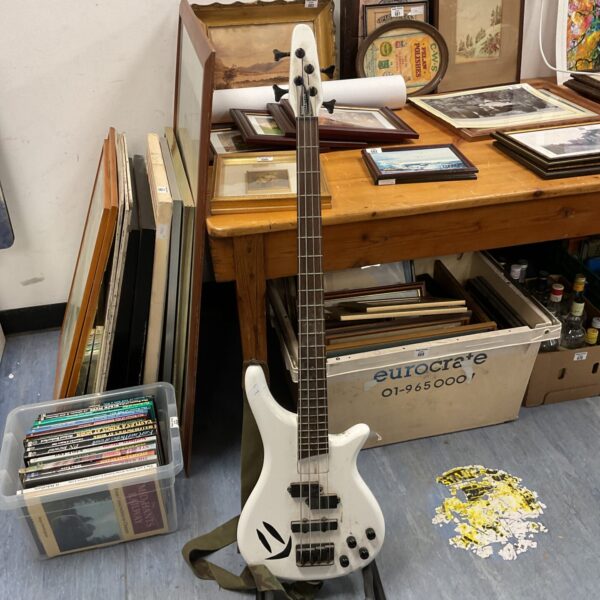White electric bass guitar displayed on a stand.