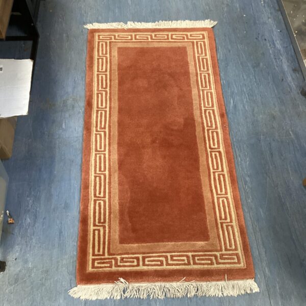 Vibrant orange Aztec rug with geometric pattern and fringed edges.