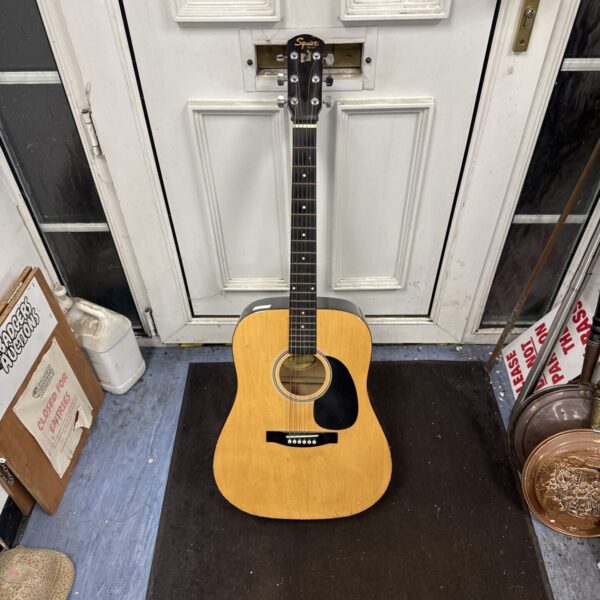 Front view of a vintage Squier acoustic guitar leaning against a door.