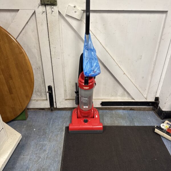 Red Vax Energise Tempo upright vacuum cleaner on a dark rug.