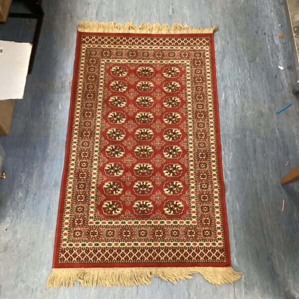 Vintage red rug with repeating pattern and fringed edges.