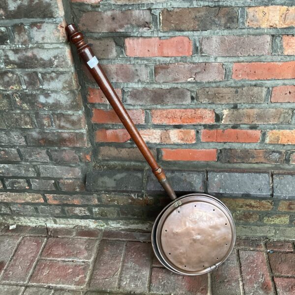 Vintage copper bed warmer with floral pattern and wooden handle.