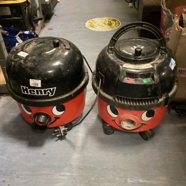 Two red Numatic Henry vacuum cleaners in a workshop setting.