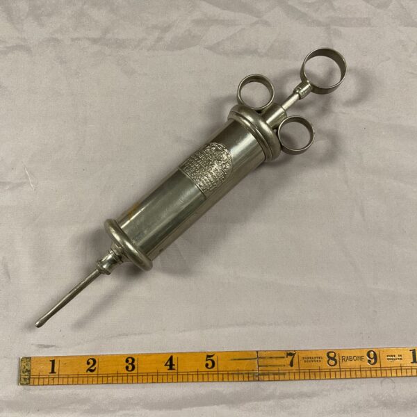 Antique Arnold & Sons surgical syringe on ruler.