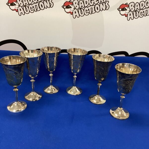 Lot of six ornate silverplate wine goblets on display.