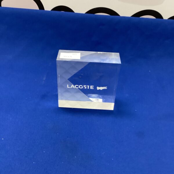 Clear Lacoste paperweight with crocodile logo on a desk.