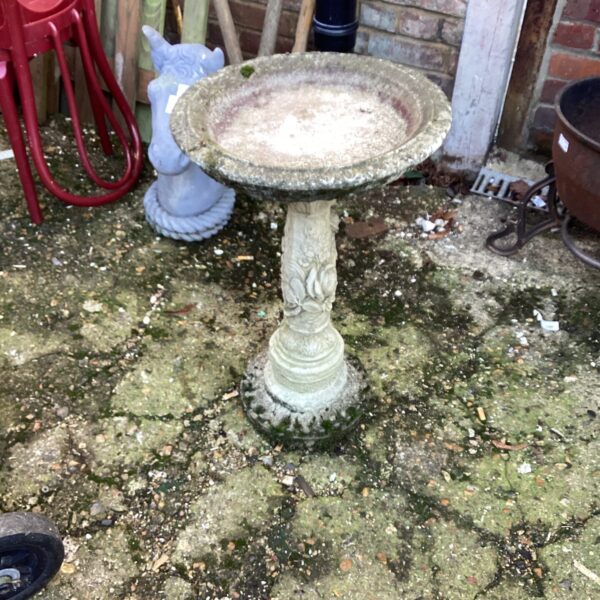 Tiered stone effect garden bird bath in a weathered garden setting.