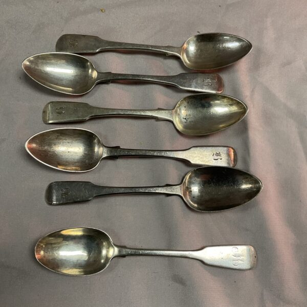 Set of six antique Georgian silver teaspoons on grey background.
