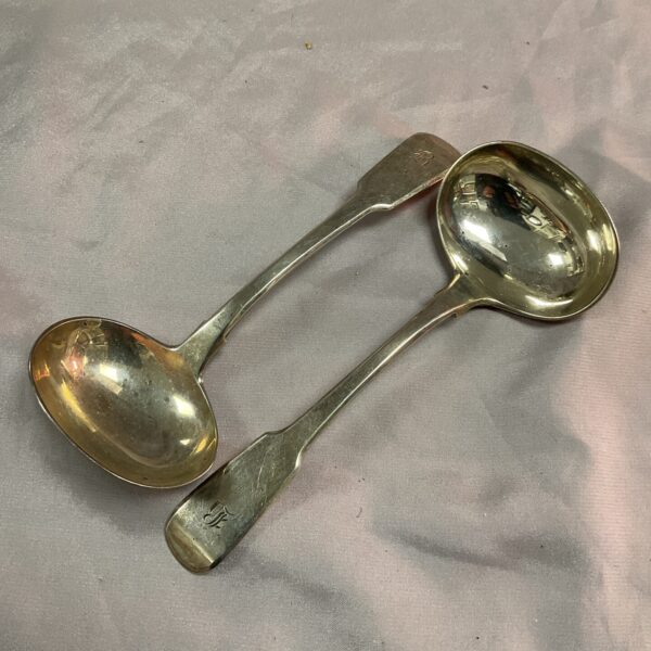 Pair of antique Georgian silver ladles on a pink background.