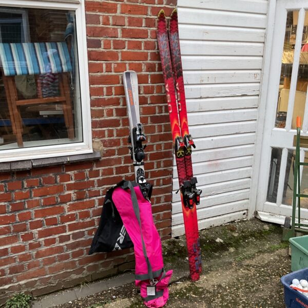 Skiing equipment lot featuring skis and a pink bag.