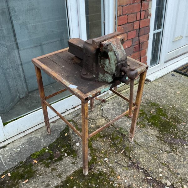 Vintage bench vice mounted on a wooden table for metalworking.
