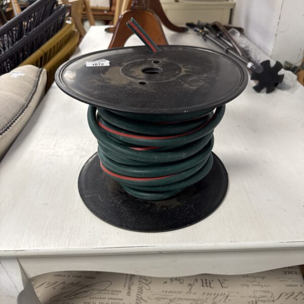 Dark rubber hosepipe coiled for storage in a garden setting.