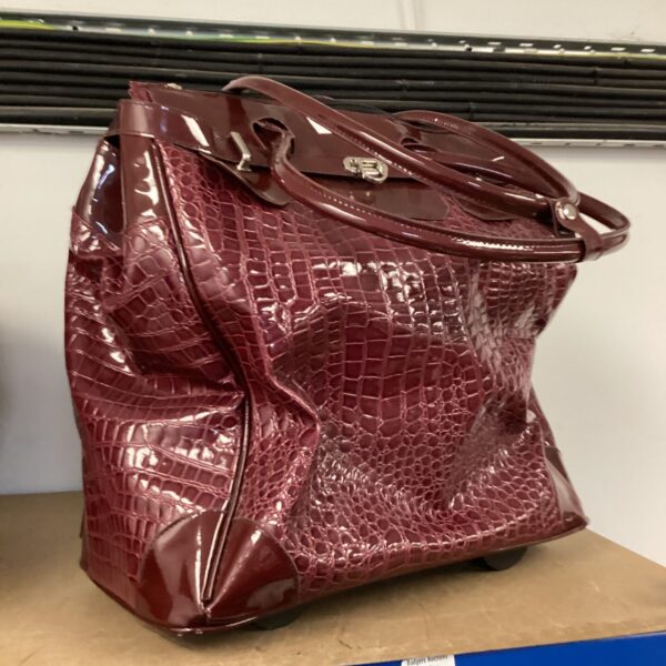 Burgundy faux croc skin bag on wheels for travel.
