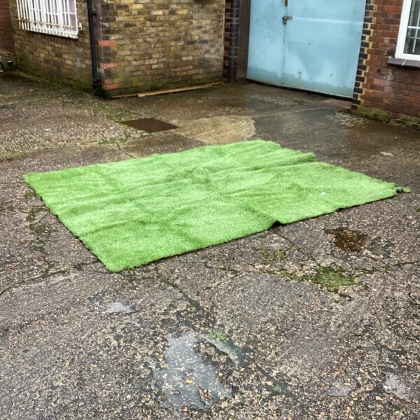 Green artificial turf laid on a paved surface in a garden setting.